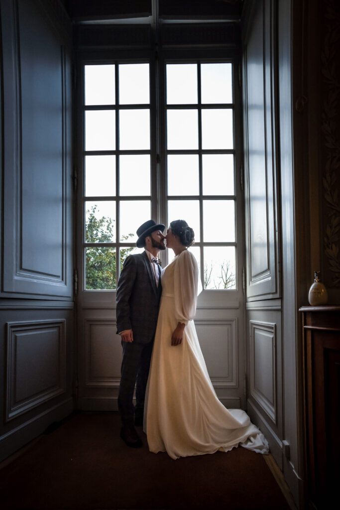 séance couple, les mariés s'embrassent devant une fenêtre du château Colbert à Maulévrier en Maine et Loire